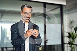 Smiling older busy business man using mobile cell phone standing in office.