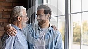 Smiling older father and adult son hug at home