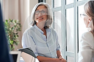 Smiling older female coach teacher communicating with students or interns