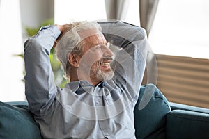 Smiling older man relaxing on couch, dreaming, looking into distance