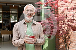 Smiling older middle aged man using phone standing outdoors.