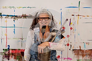 Smiling older woman, proud artist, in her fifties with grey hair and glasses and many paintbrushes