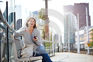 Smiling older woman sitting outside with mobile phone