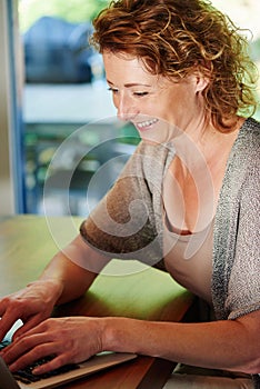 Smiling older woman typing on laptop at desk