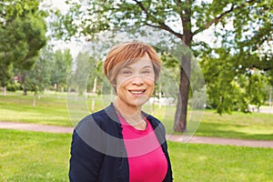 Smiling older woman walking in park. Elderly woman with red short haircut outdoors. Mature beauty