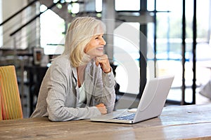 Smiling older woman working laptop computer indoors