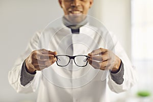 Smiling optician holds new good quality eyeglasses and suggests you try them on