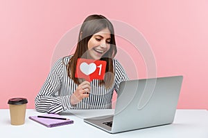 Smiling optimistic woman blogger chatting with followers on video call at laptop asking to rate her posts showing likes counter