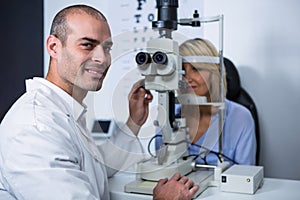 Smiling optometrist examining female patient on slit lamp