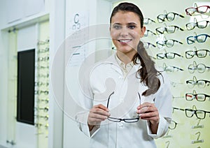 Smiling optometrist holding spectacles in optical store