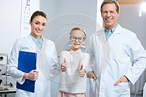 smiling optometrists and little kid in eyeglasses showing