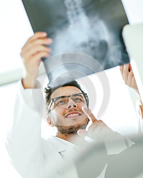 Smiling orthopedist doctor looks at the x - ray of the patient photo