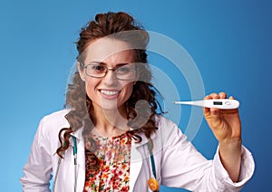 Smiling paediatrician doctor showing thermometer on blue