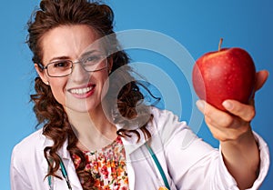 Smiling paediatrician woman giving an apple on blue