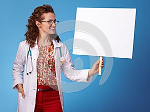 Smiling paediatrician woman looking at placard on blue photo
