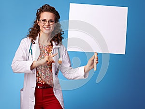 Smiling paediatrician woman pointing at placard on blue