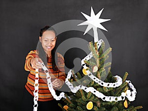 Smiling Papuan girl putting white paper chain on Christmas tree