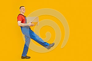 Smiling parcel delivery man carrying box isolated on yellow background. Courier with the parcel takes step. Full-length portrait.