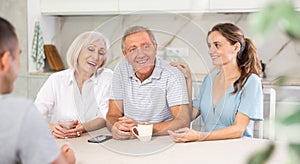 Smiling parents and adult children sit at the table with tea and talk about home life