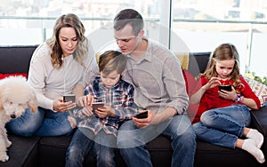 Smiling parents with children spending time playing with smartphones