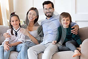 Smiling parents with kids relax on couch at home