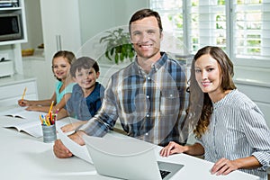 Smiling parents working with laptop and childrens studying in living room at home