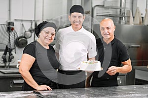 Smiling pastry Chefs team showing a cake. Bakery workgroup. Chef team.