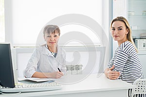 Smiling patient receiving a medical consultation and looking at camera, the female doctor is sitting at desk on the