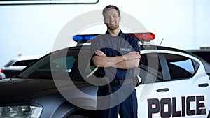 Smiling patrolman standing near car with crossed hands, carrying out duties photo