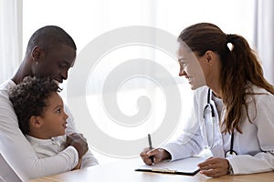 Smiling pediatrician doctor talking to African American child at meeting