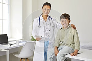 Smiling pediatrician doctor woman is cuddling teen boy on appointment in clinic with care.