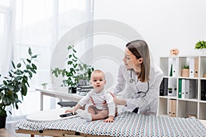 Smiling pediatrician holding baby near scales