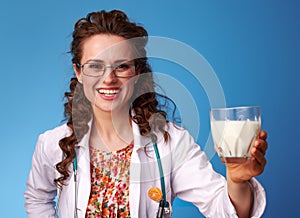 Smiling pediatrist doctor giving glass of milk on blue photo