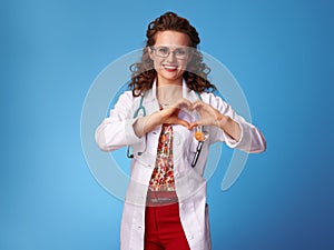 Smiling pediatrist doctor showing heart shaped hands on blue photo