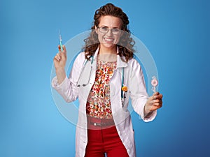 Smiling pediatrist doctor with syringe and lollypop on blue photo