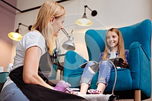 Smiling pedicurist talking to her client while doing pedicure