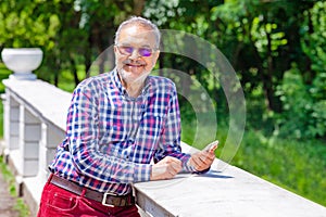 Smiling Pensioner with Casual Clothing and Glasses and Phone in Park