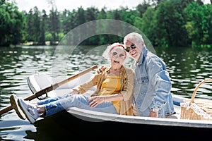 Smiling pensioners sitting in little boat while having romantic date