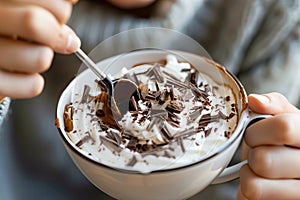smiling person stirring a cup of coffee, chocolate shavings on whipped cream