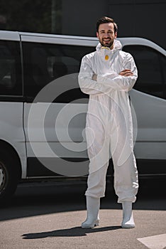 smiling pest control worker with crossed arms looking at camera near car