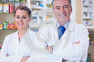 Smiling pharmacist and his trainee with arms crossed