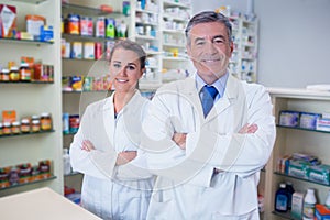 Smiling pharmacist and his trainee with arms crossed