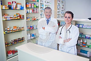 Smiling pharmacist and his trainee with arms crossed