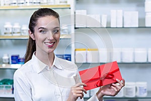 Smiling pharmacist holding present in pharmacy