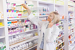 Smiling pharmacist phoning and taking medicine from shelf photo