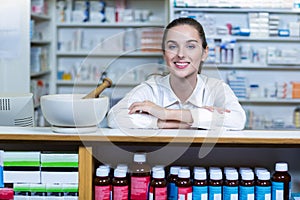 Smiling pharmacist sitting at counter in pharmacy