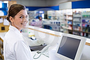 Smiling pharmacist standing at counter in pharmacy