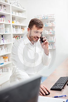 Smiling pharmacist talking on the phone and working on a computer