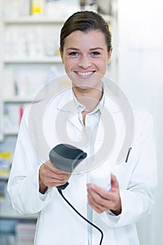 Smiling pharmacist using barcode scanner on medicine bottle in pharmacy