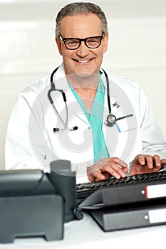 Smiling physician in eye wear typing on keyboard